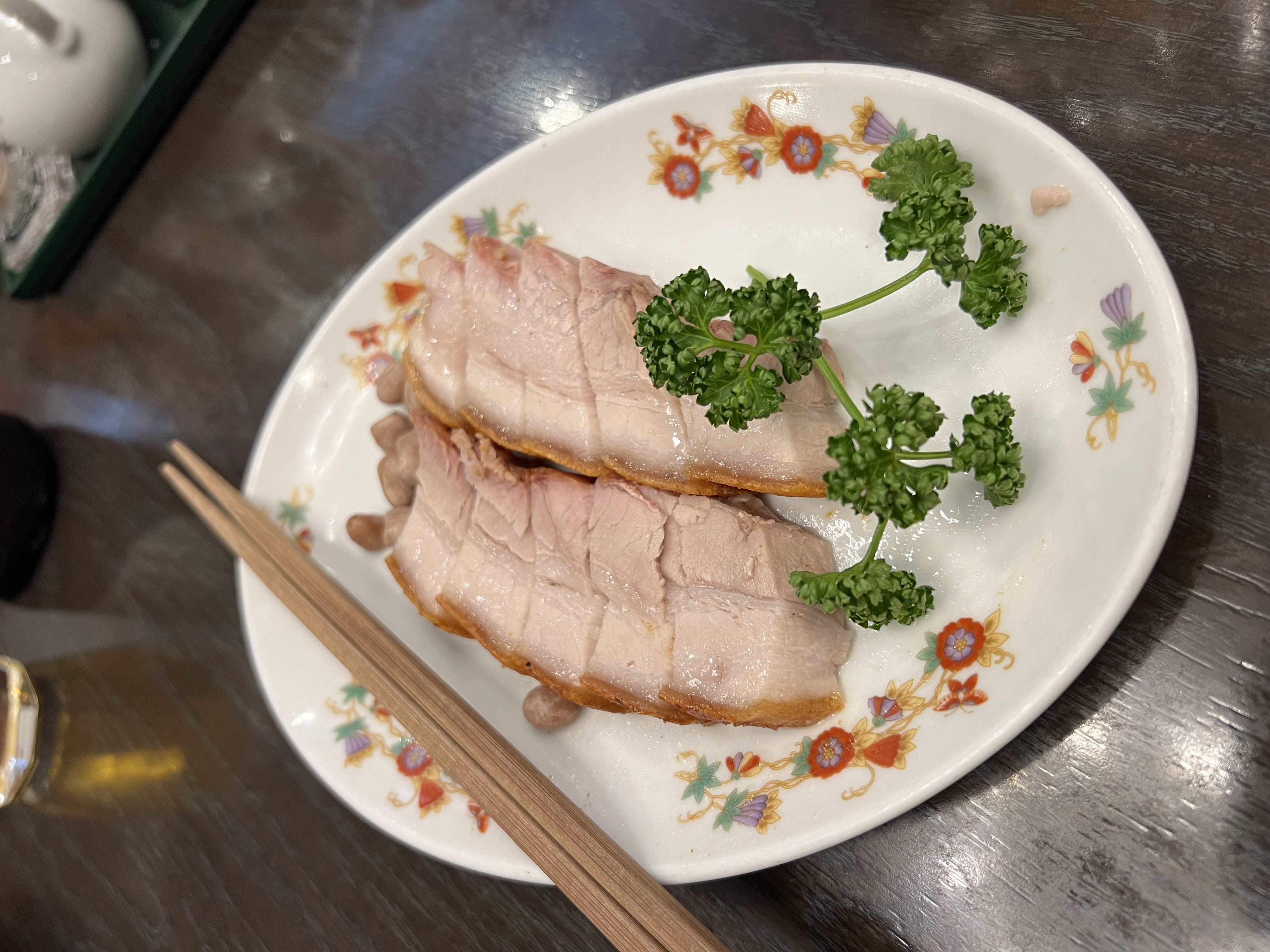Sliced roast pork on a floral plate with chopsticks